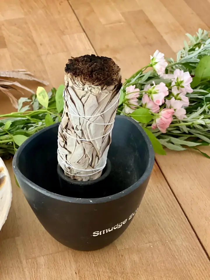 Räucherbündel in einer schwarzen Schale, daneben frische Kräuter und Blüten