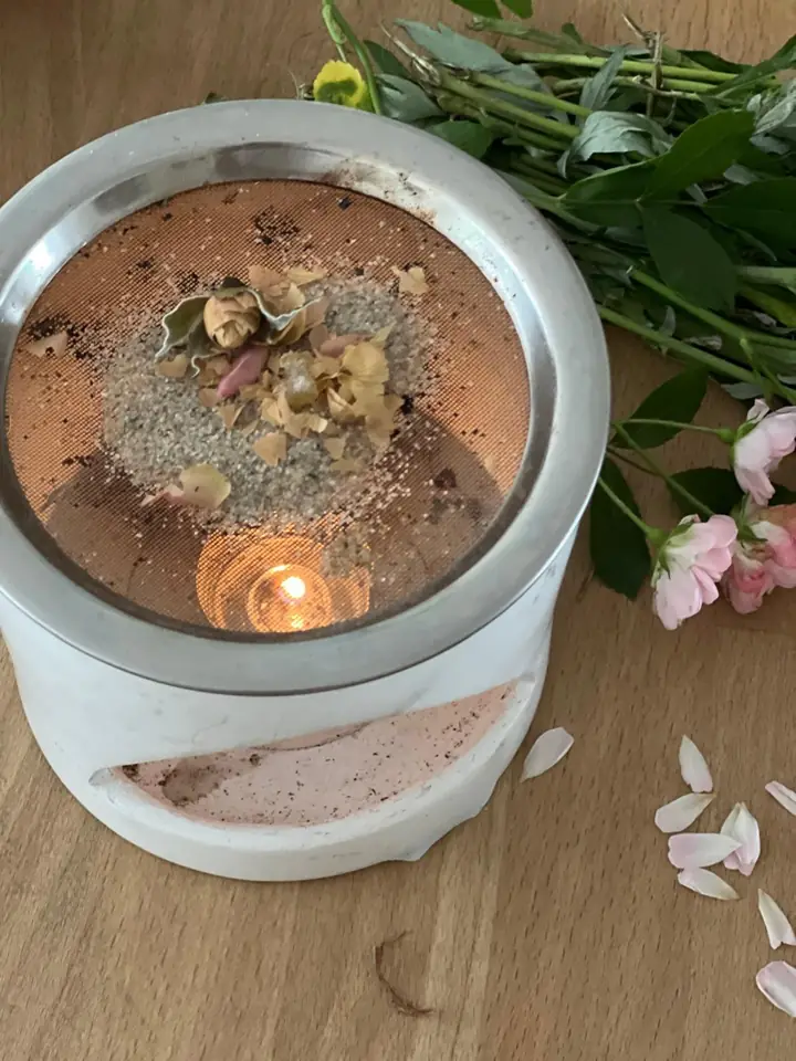Stövchen mit Kräutern und Blüten auf dem Sieb über einem Teelicht